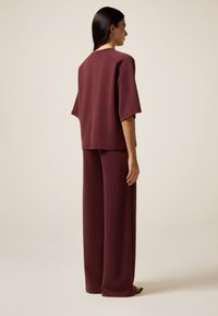 Maroon-kleurige loungeset met een losse top met korte mouwen en wijde broekspijpen, gemaakt van zachte, gestructureerde stof.