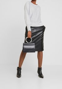 Maglione grigio a maglia, gonna a matita in pelle nera, borsa nera con manico circolare e stivaletti neri. Texture lisce, design aderente.