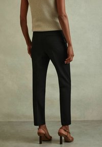 Černé kalhoty na míru se slim fit střihem, se zadními kapsami. Kombinované se světle béžovým pleteným topem a hnědými sandály na podpatku.