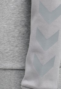 Felpa grigia con una texture morbida, con un bordo grigio scuro all'orlo e tre motivi a chevron in un grigio più chiaro sulla manica.