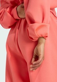 Korálovo ružový overal vyrobený z mäkkej tkaniny, s objemnými rukávmi, elastickými manžetami a priliehavým siluetou zvýraznenou v páse.