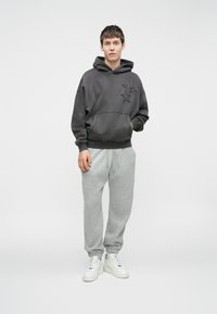 Moleton cinza escuro com bordados de estrelas, combinado com calças de treino cinza claro e ténis brancos. Material suave e corte descontraído.