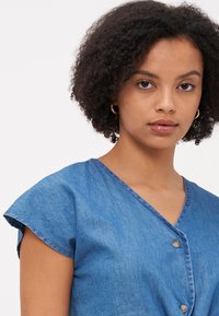 Vestido de ganga azul com decote em V, mangas curtas e fecho frontal com botões. Textura suave com um corte e acabamento clássicos.