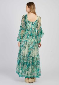 Robe maxi en tissu transparent à motif floral comprenant des nuances de vert et de bleu. Manches longues et évasées, avec un détail de jupe à volants.