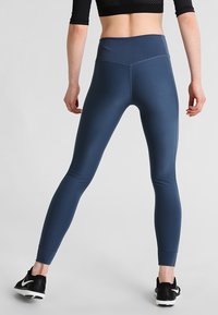 Leggings taille haute bleu marine en tissu extensible, dotés d'une ceinture côtelée et d'un design ajusté avec des poignets aux chevilles. Chaussures de sport noires.