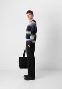 Gestreifter Pullover aus Wolle mit horizontalen Streifen in Marineblau und Grau, Rundhalsausschnitt und einem Logopatch am linken Ärmel. Kombiniert mit schwarzen Hosen und einer Tasche.