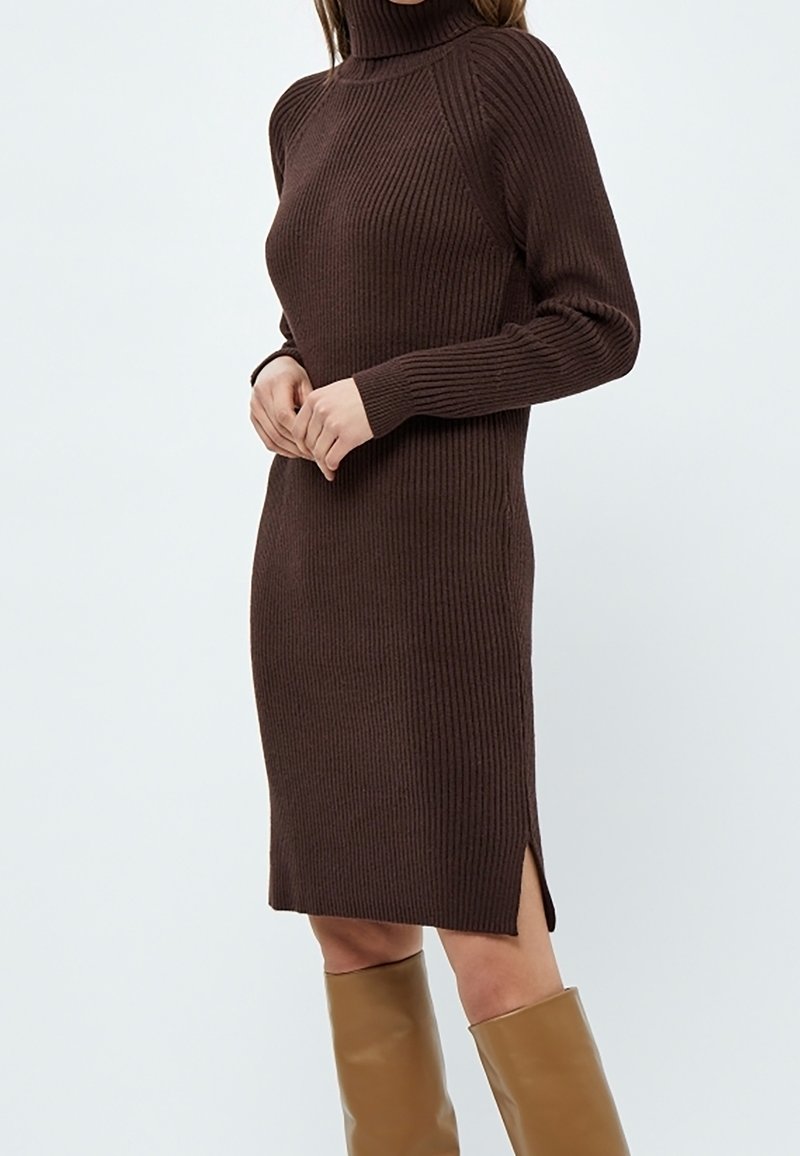 Robe en tricot marron côtelé avec un col roulé ajusté, des manches longues et des fentes latérales, accompagnée de bottes beige montant jusqu'aux genoux.