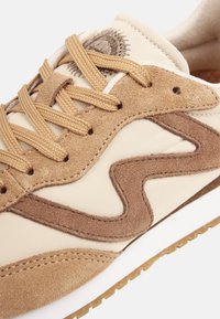 Beiger Sneaker aus Wildleder und synthetischem Material, mit braunen Akzenten, strukturierten Überzügen und beigen Schnürsenkeln. Weiße Sohle mit Gummilaufsohle.