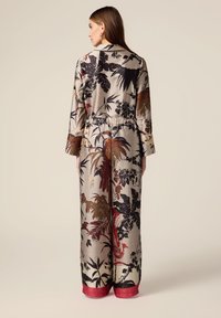 Langer, gemusterter Jumpsuit mit einer Mischung aus erdigen Farbtönen und botanischen Druckmotiven, mit einer taillierten Taille und kontrastierenden roten Bündchen am Saum.