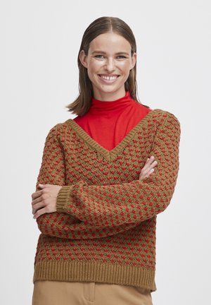 Gebreide trui in bruin, met een V-hals en een textuurpatroon met rode accenten. Geribbelde manchetten en zoom, gedragen over een rode coltrui.