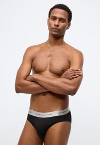 Μαύρα βαμβακερά σλιπάκια με γκρι ελαστική ζώνη μέσης που φέρει το λογότυπο "TOMMY HILFIGER". Η εφαρμογή είναι στενή και ο σχεδιασμός μινιμαλιστικός.