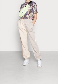 Lichte joggers in beige en crème met zijaccenten in kleur. Gecombineerd met een bloemetjespatroon cropped shirt en een mintgroene crossbody tas.