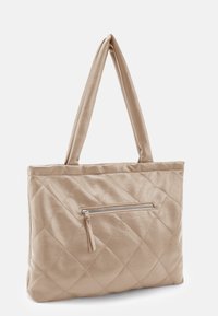 Sac fourre-tout matelassé beige en cuir lisse. Il est équipé de deux longues anses et d'une poche avant zippée avec un pompon en guise de tirette.