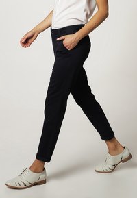 Granatowe, dopasowane spodnie z miękkiego materiału, z podwińcem i bocznymi kieszeniami. W połączeniu z białymi butami z wycięciami.