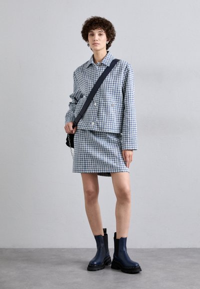 Modrá a biela houndstooth bunda s voľným strihom, skombinovaná s vyhovujúcou sukňou. Čierne členkové čižmy s robustnou podrážkou dotvárajú celkový vzhľad.
