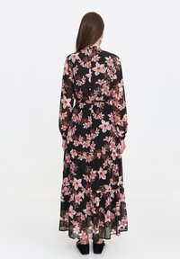 Long black dress with floral pink and green print, sheer fabric, long sleeves, waist tie, and tiered skirt. Simple neckline and flowing design.
