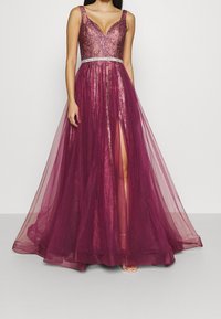 Długa bordowa wieczorowa sukienka z dopasowanym gorsetem, dekoltem w kształcie litery V, ozdobnymi detalami oraz przezroczystą, warstwową spódnicą z rozcięciem do uda.