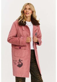 Ružový kordový kabát s hnedým umelým kožúškom, na vrecku s grafickým motívom jablka a textom. Dva predné gombíky a veľké vrecká.