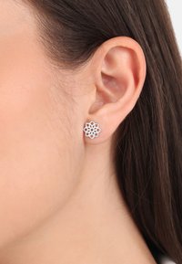 Los pendientes de botón plateados presentan un intrincado diseño de corte. Tienen un acabado pulido y una forma simétrica, similar a una flor.