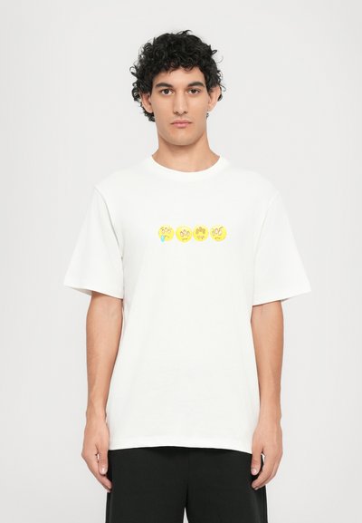 T-shirt bianco in cotone con una grafica centrale che presenta quattro faccine gialle sorridenti con diverse espressioni. Vestibilità ampia e maniche corte.