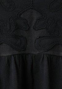 Tissu noir avec des formes abstraites brodées et des panneaux en mesh se fondant dans un tissu froncé en dessous.
