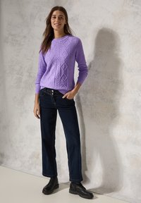 Pull en tricot violet avec texture côtelée et motifs en diamant, associé à un jean large bleu foncé et des bottes noires à lacets.