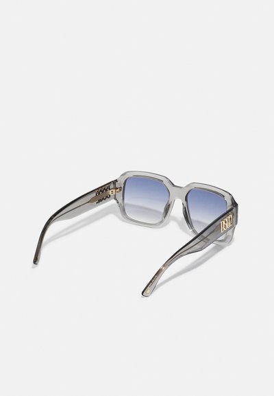 Ochelari de soare cu rame clare, cu o formă geometrică, lentile gradiente de culoare albastră și accente aurii pe brațe. Textură netedă cu linii de design distincte.
