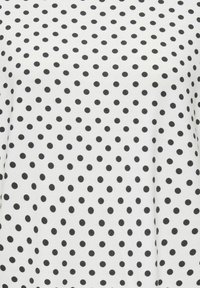 Tissu blanc avec des petits pois noirs espacés uniformément formant un motif régulier.