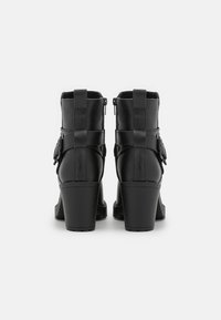 Bottines noires à talon épais, en matériau synthétique texturé, avec des zips latéraux et des boucles décoratives à l'extérieur.