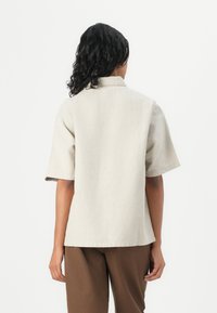 Beige short-sleeve shirt with a collar, made of lightweight fabric. Straight fit, simple design, finished with stitched hem details.