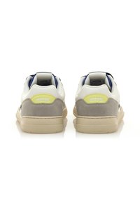 Weiß-graue Sneakers mit einer strukturierten Plattform, die an der Ferse einen gelben Akzent und einen marineblauen Saum um den Kragen haben.