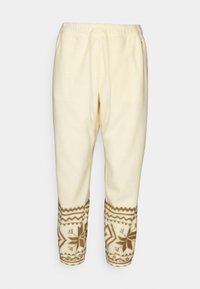 Krämfärgade sweatpants med bruna geometriska mönster vid mudden. Tillverkade av mjukt material med elastisk midja och dragsko.