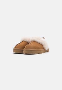 Pantoufles en suede marron à enfiler avec un poignet en fourrure blanche et une semelle en caoutchouc texturée. Fini lisse, design à bout arrondi.