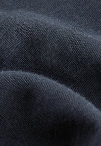 Fekete textil, puha, textúrált szövettel, amely redőket és ráncokat mutat, jelezve a rugalmasságot és a könnyű anyagot.