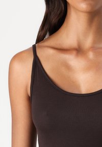 Débardeur marron à côtes avec des fines bretelles et un décolleté dégagé, mettant en valeur une texture de tissu lisse et une coupe ajustée.