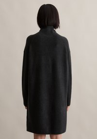 Temno siva pletena obleka s visokim ovratnikom, raglan rokavi in ribastimi manšetami. Mehka tekstura z sproščenim, večjim krojem.