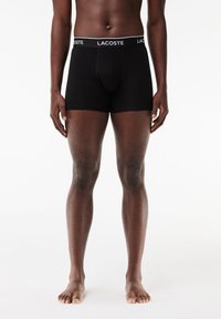 Black boxer briefs with a branded elastic waistband displaying "LACOSTE." Made from a smooth fabric, featuring a contoured pouch.