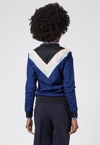 Navy bomber jacket with black and cream geometric color-blocking. Features a ribbed collar and cuffs, smooth fabric with a glossy finish.
