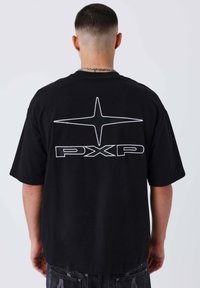 Camiseta de algodón negra de corte grande con un gráfico de estrella blanca y el texto "PXP" en la espalda. Mangas cortas y un ajuste holgado.