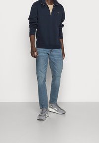 Marine sweatshirt met een half-rits ontwerp, gecombineerd met lichtblauwe jeans en grijze sneakers. Heeft geribbelde boorden en een klein logo op de borst.