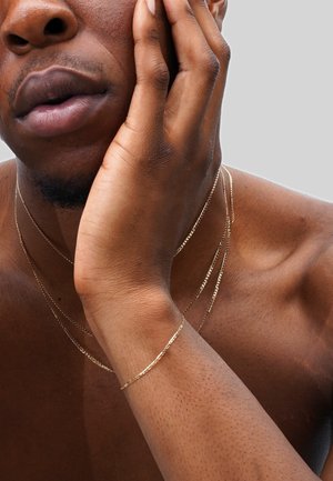 Gold-tone layered necklaces, thin chain design, varying lengths, textured surfaces, resting on a brown skin tone.