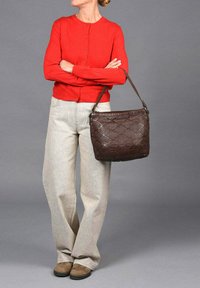 Bolso de cuero trenzado marrón con acabado texturizado, una correa resistente y forma redondeada. Combinado con un cárdigan rojo y pantalones de pierna ancha beige.