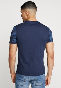Navy blue t-shirt with short sleeves, featuring a tropical print on the shoulders. Made of cotton with a smooth texture.