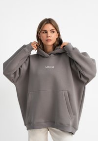 Grauer oversized Hoodie aus weichem Stoff. Mit Kängurutasche, verstellbarem Kordelzug an der Kapuze und gesticktem Logo auf der Brust.