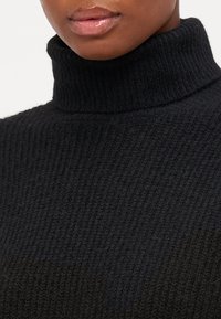 Czarny prążkowany sweter z golfem, wykonany z teksturowanej tkaniny, z wysokim kołnierzem i subtelnym gradientem przechodzącym od jasnego do ciemnego odcienia.