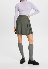 Grauer plissierter Rock mit karriertem Muster, kombiniert mit einem helllila Rollkragenpullover und grauen knielangen Socken, abgerundet mit schwarzen Slippern.