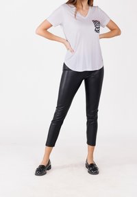 Camiseta de manga corta gris claro con un bolsillo de estampado de leopardo, combinada con leggings ajustados de cuero sintético negros y mocasines negros.