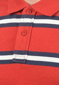 Rotes Polohemd mit Kragen, mit horizontalen Streifen in Marineblau und Weiß, zwei roten Knöpfen und sichtbaren Nähdetails.