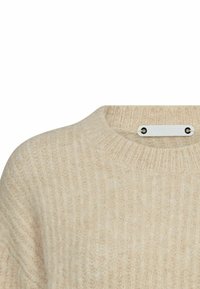 Beżowy sweter dzianinowy o prążkowanej strukturze, z okrągłym dekoltem i metalową metką z dwoma czarnymi wkrętami z tyłu.