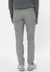 Pantalones de cuadros grises con corte ajustado, que cuentan con dos bolsillos traseros y detalles de botones. El material parece suave con un patrón a cuadros.